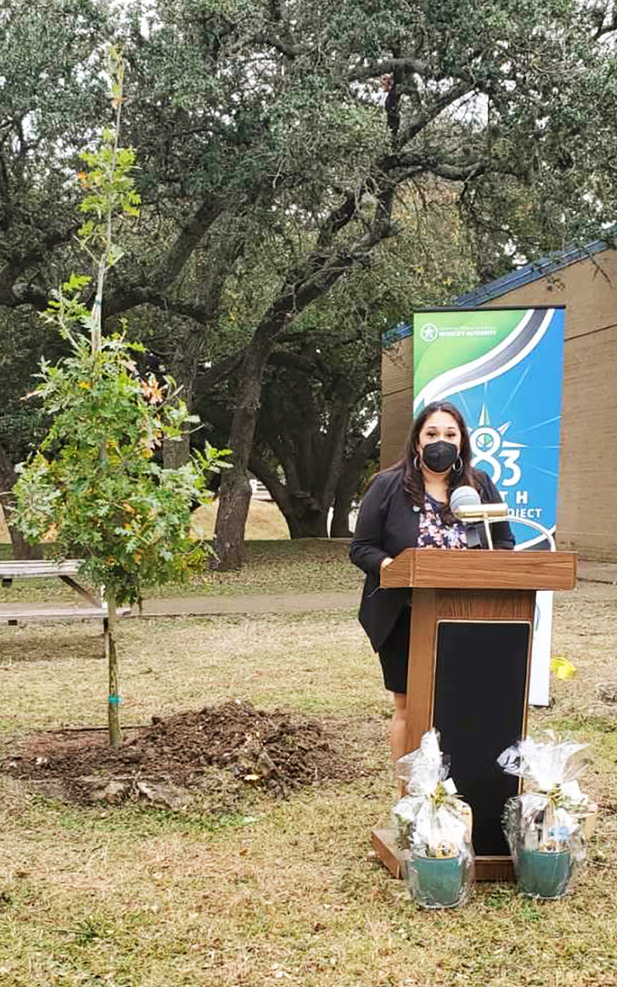 Principal Amanda Serna-Castro delivers remarks from a podium next to a newly-planted tree on the Grisham Middle School grounds.